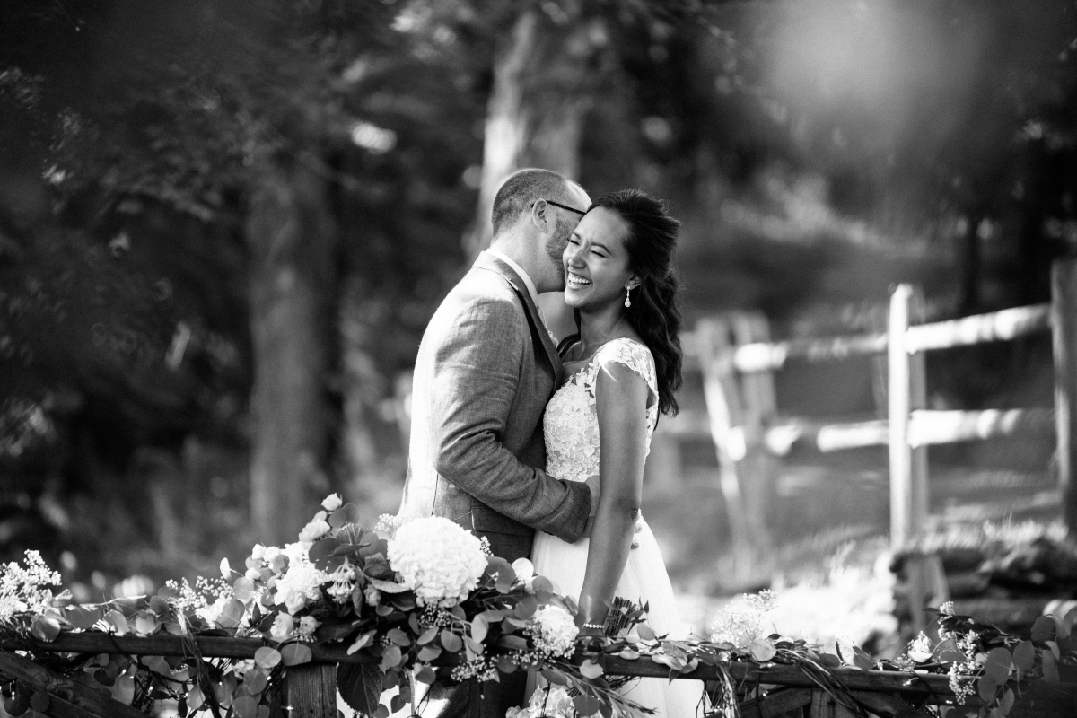 Black and white happy bride and groom candid natural laughing bridge Sunny day sunshine Flower trellis archway Inn at Millrace Pond New Jersey Rustic Intimate Summer Wedding Yellow Flowers Bouquet Happy Candids Bride and Groom