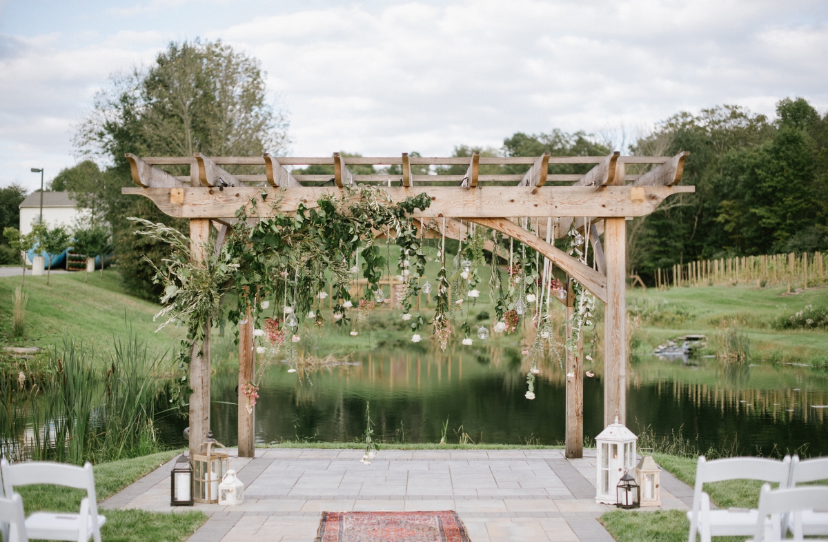 beautiful ceremony floral arrangements trellis hanging plants hanging candles rustic wood by the water lanterns outdoors Bear Brook Valley Wedding