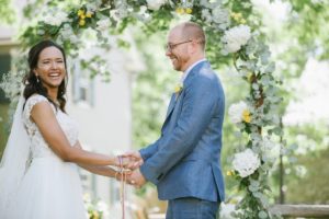 happy holding hands traditions Sunny day sunshine Flower trellis archway Inn at Millrace Pond New Jersey Rustic Intimate Summer Wedding Yellow Flowers Bouquet Happy Candids Bride and Groom