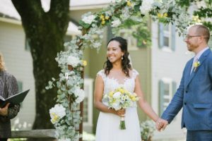 holding hands ceremony Sunny day sunshine Flower trellis archway Inn at Millrace Pond New Jersey Rustic Intimate Summer Wedding Yellow Flowers Bouquet Happy Candids Bride and Groom
