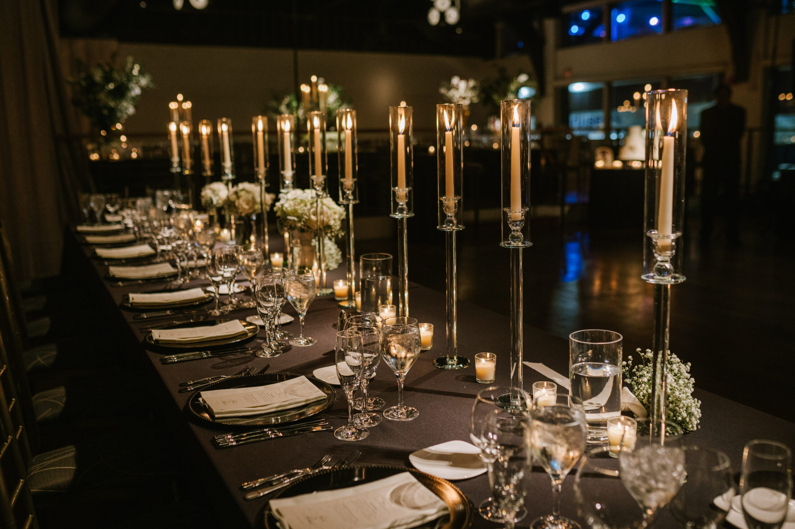 An elegant NYC wedding reception at Chelsea Piers, with long tables with black linens, tall glass candleholders, and lush floral arrangements.