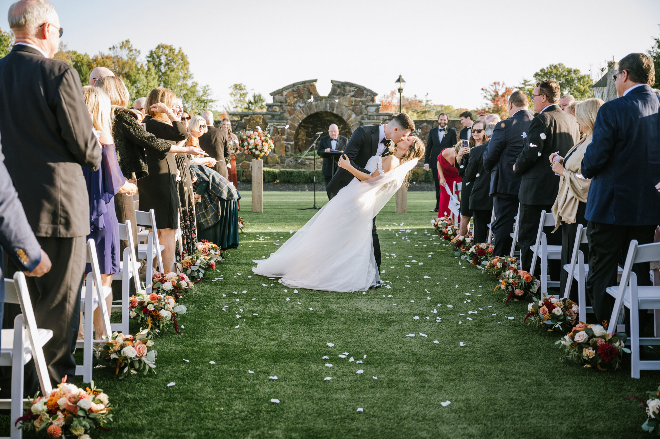 Couple sharing a kiss at the end of their outdoor ceremony at The Tillinghouse wedding venue in Monmouth County, NJ, surrounded by rows of autumn floral arrangements and happy guests