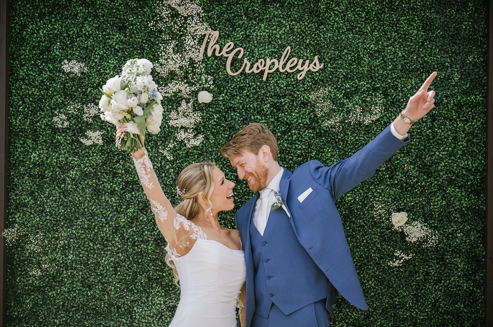 Bride and groom celebrating in front of a green floral wall at The Hamilton Manor wedding venue in New Jersey.